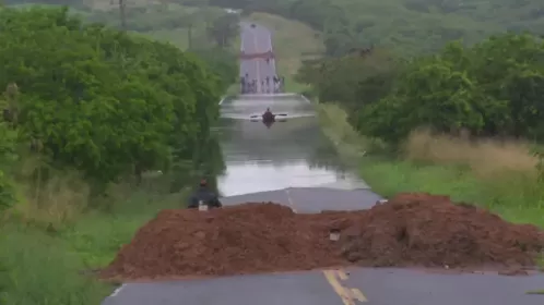 Barragem transborda por causa das chuvas, ponte fica submersa e moradores atravessam de barco